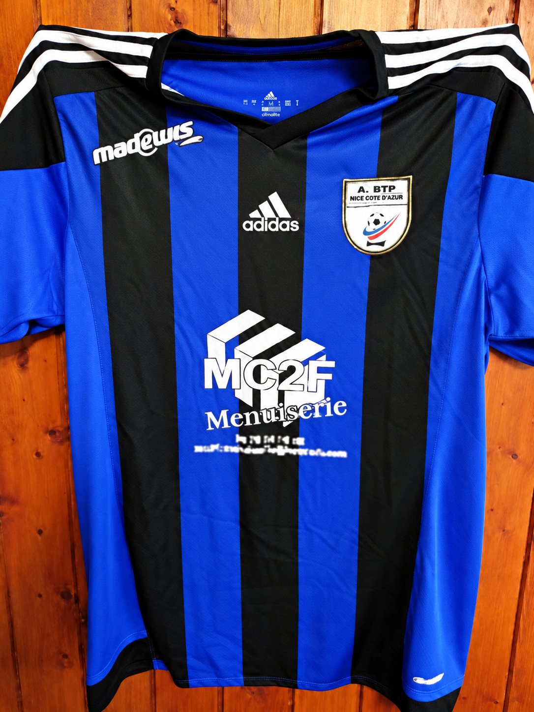 Maillot de football bleu et noir portant le sponsor MC2F Menuiserie