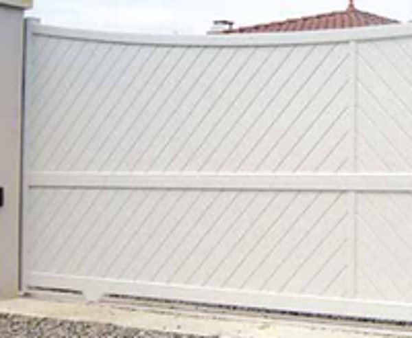 Un grand portail coulissant blanc à lames posées en diagonale, installé devant une maison au toit de tuiles.