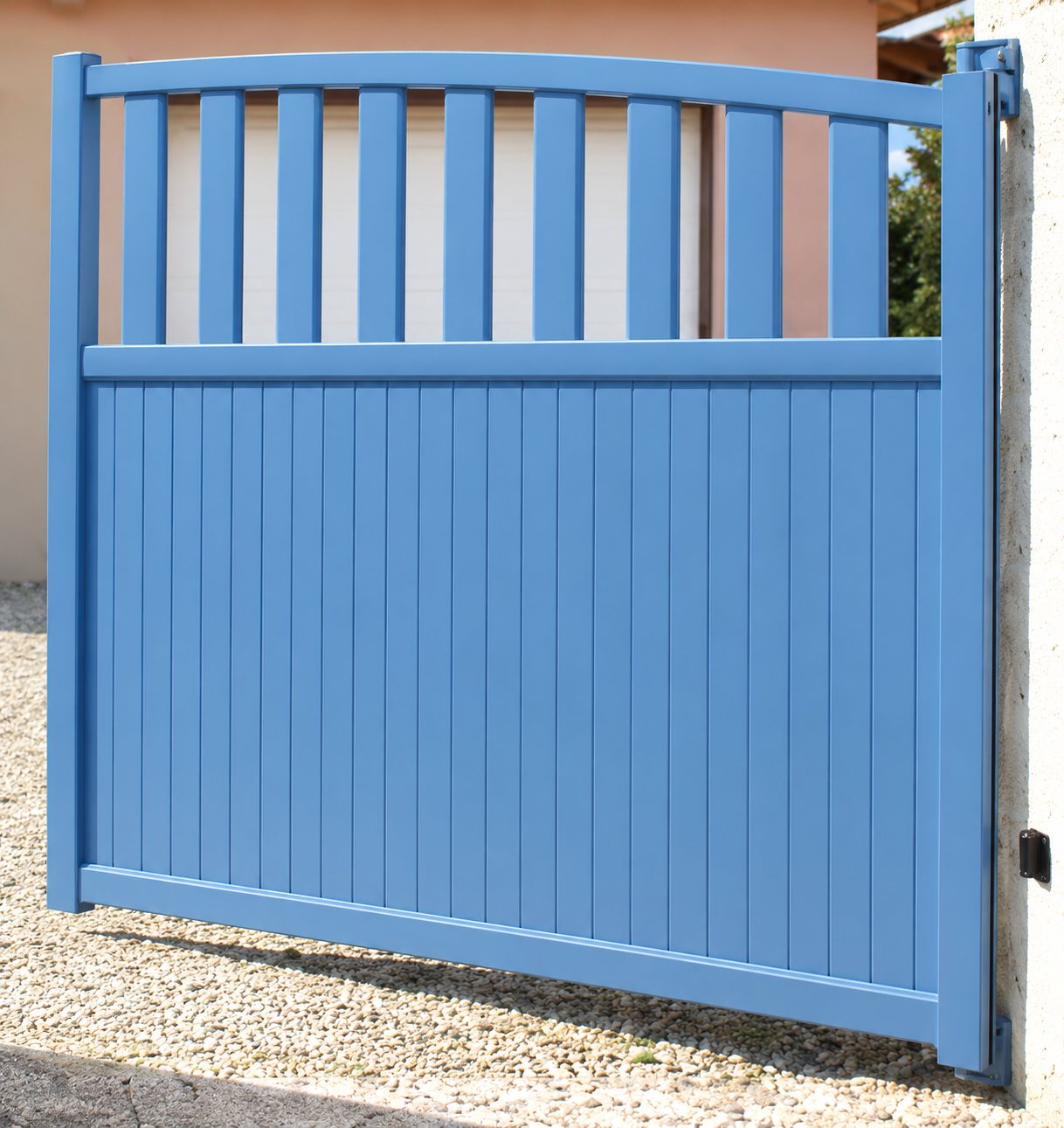 Un portail bleu à lames verticales, dont la partie haute est ajourée, installé devant une maison.