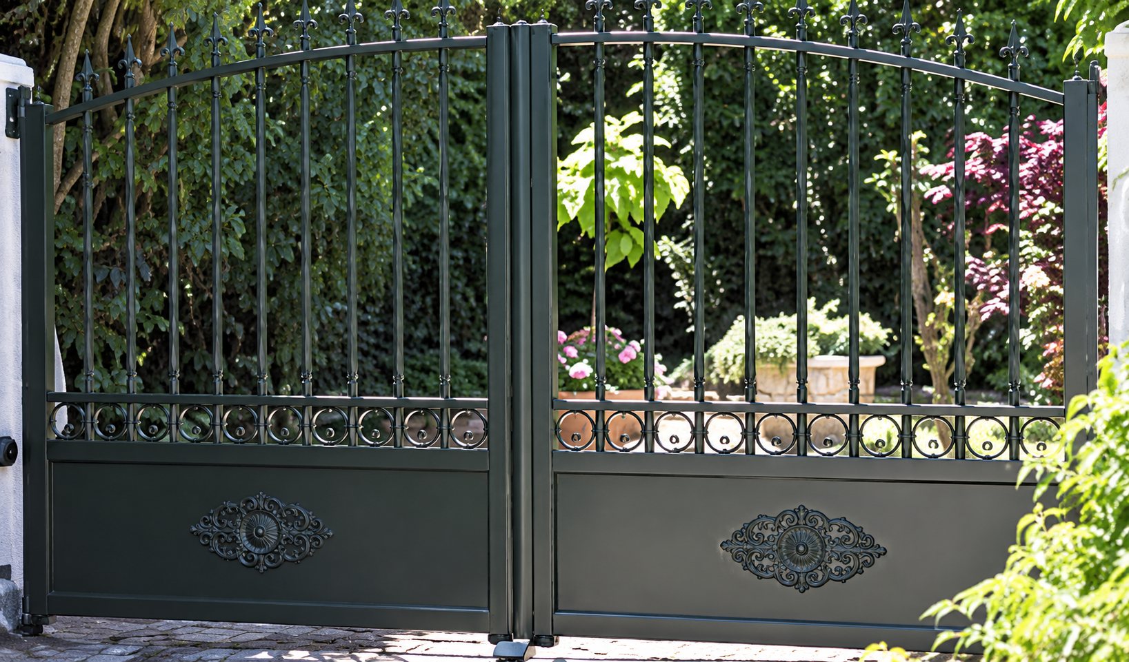 Un portail en métal noir à deux battants aux barreaux ouvragés laisse entrevoir un jardin fleuri derrière une clôture.