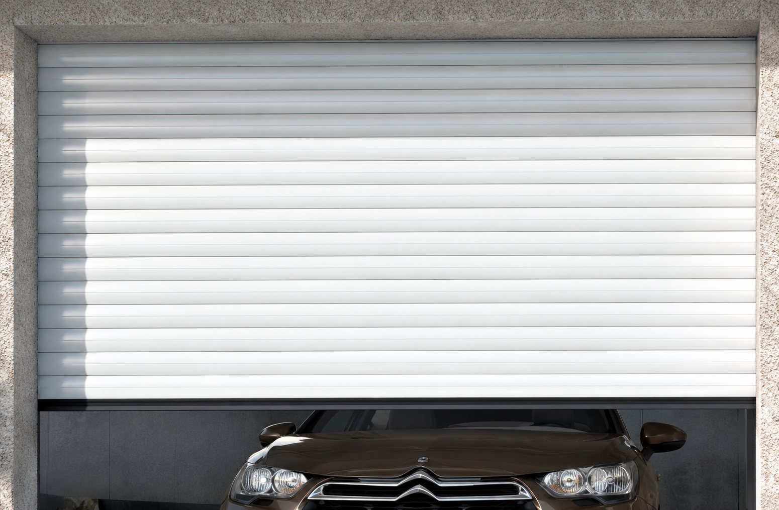 Une porte de garage enroulable blanche à lamelles est à moitié relevée et laisse apparaître l'avant d'une voiture sombre.